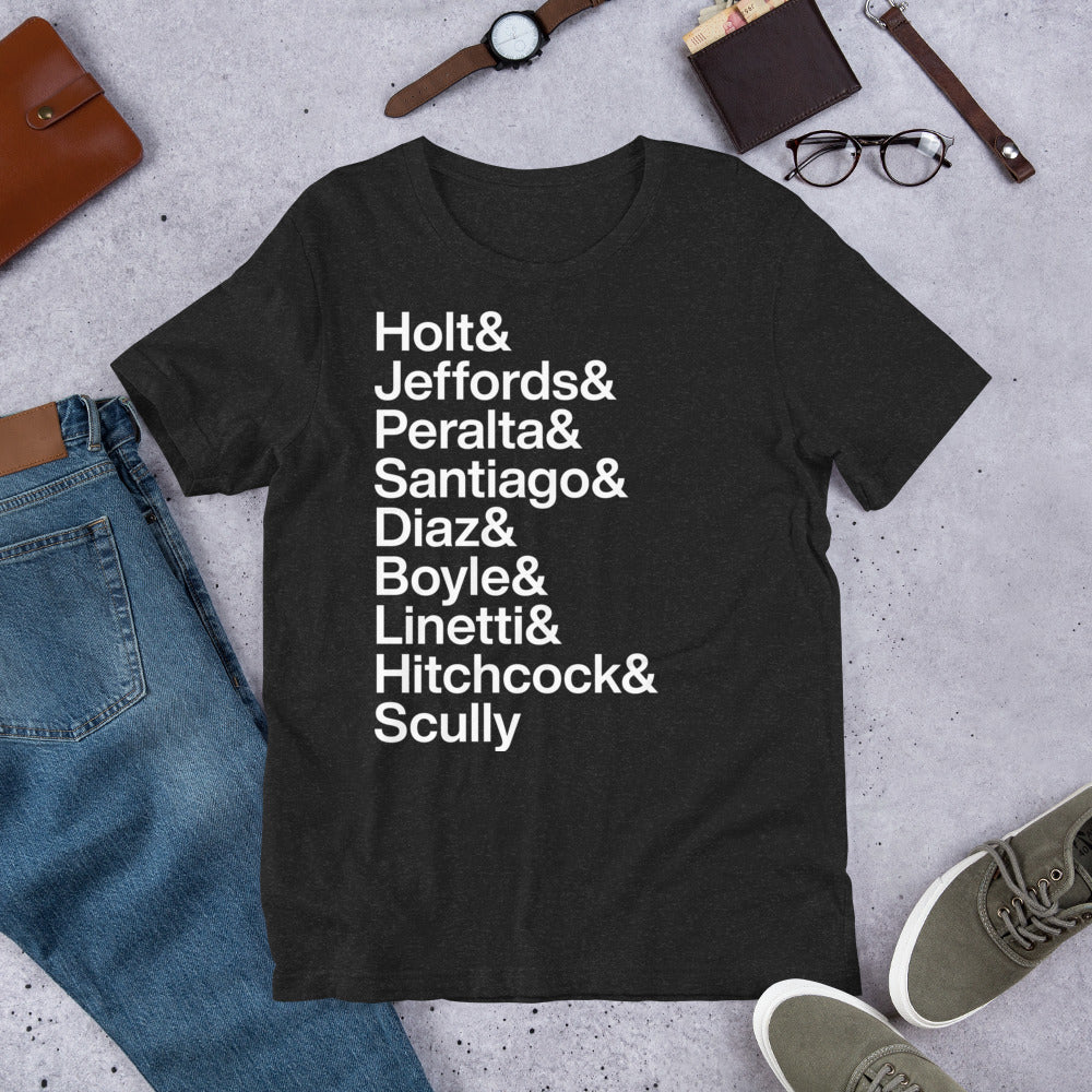 black t-shirt with white lettering reading Holt and Jeffords and Peralta and Santiago and Diaz and Boyle and Linetti and Hitchcock and Scully on the ground with other apparel
