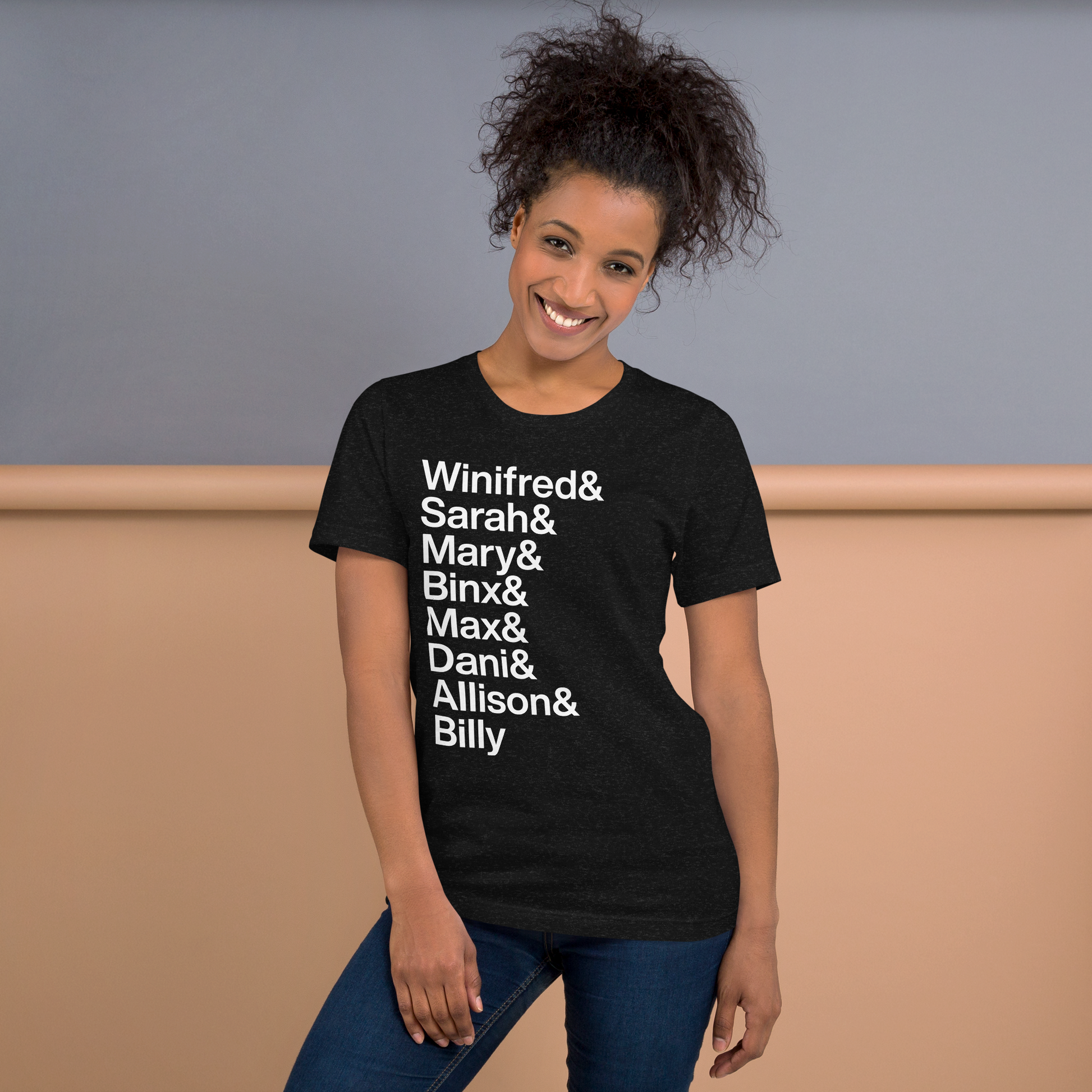 Young woman wearing black t-shirt with white lettering displaying "Winifred and Sarah and Mary and Binx and Max and Dani and Allison and Billy"