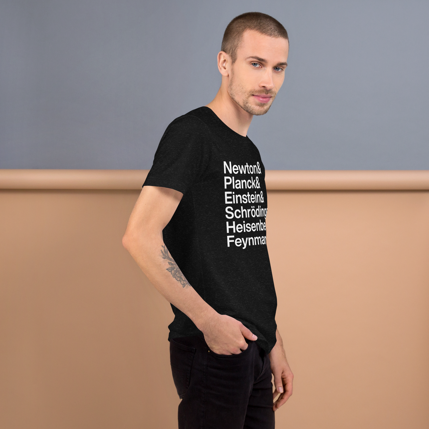 Tattooed young man wearing black t-shirt with white lettering reading Newton and Planck and Einstein and Shrodinger and Heisenberg and Feynman