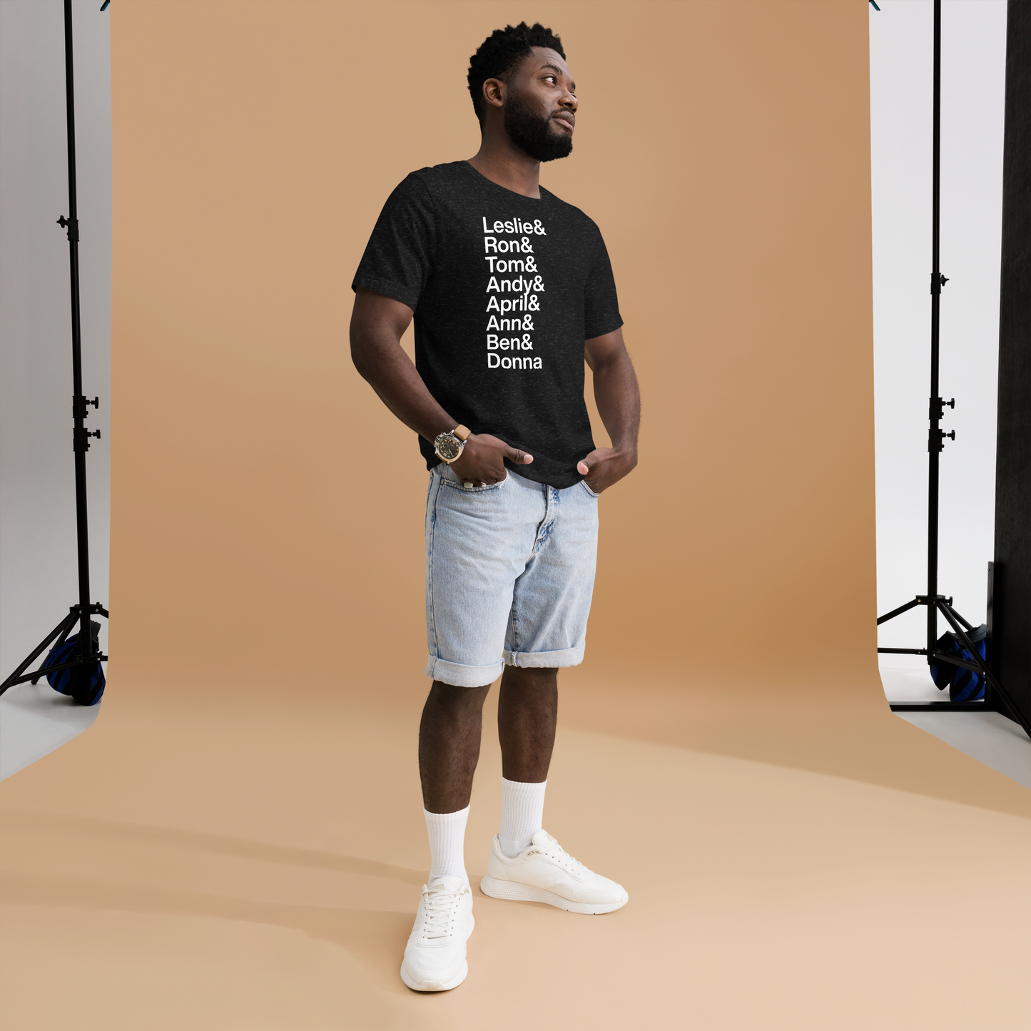 Man posing in a black t-shirt with white lettering reading Leslie and Ron and Tom and Andy and April and Ann and Ben and Donna