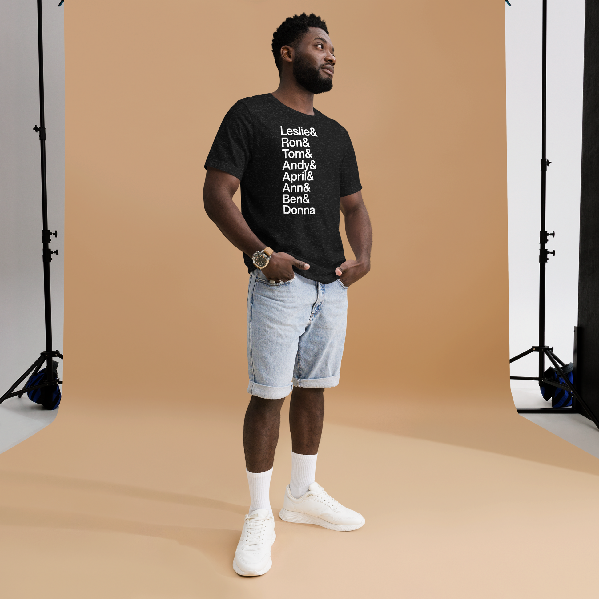 Man posing in a black t-shirt with white lettering reading Leslie and Ron and Tom and Andy and April and Ann and Ben and Donna