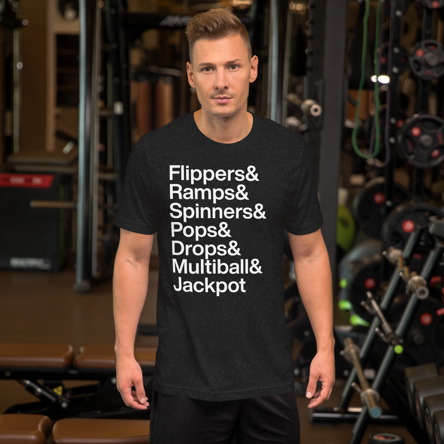 Man in gym wearing black t-shirt with white lettering reading Flippers and Ramps and Spinners and Pops and Drops and Multiball and Jackpot
