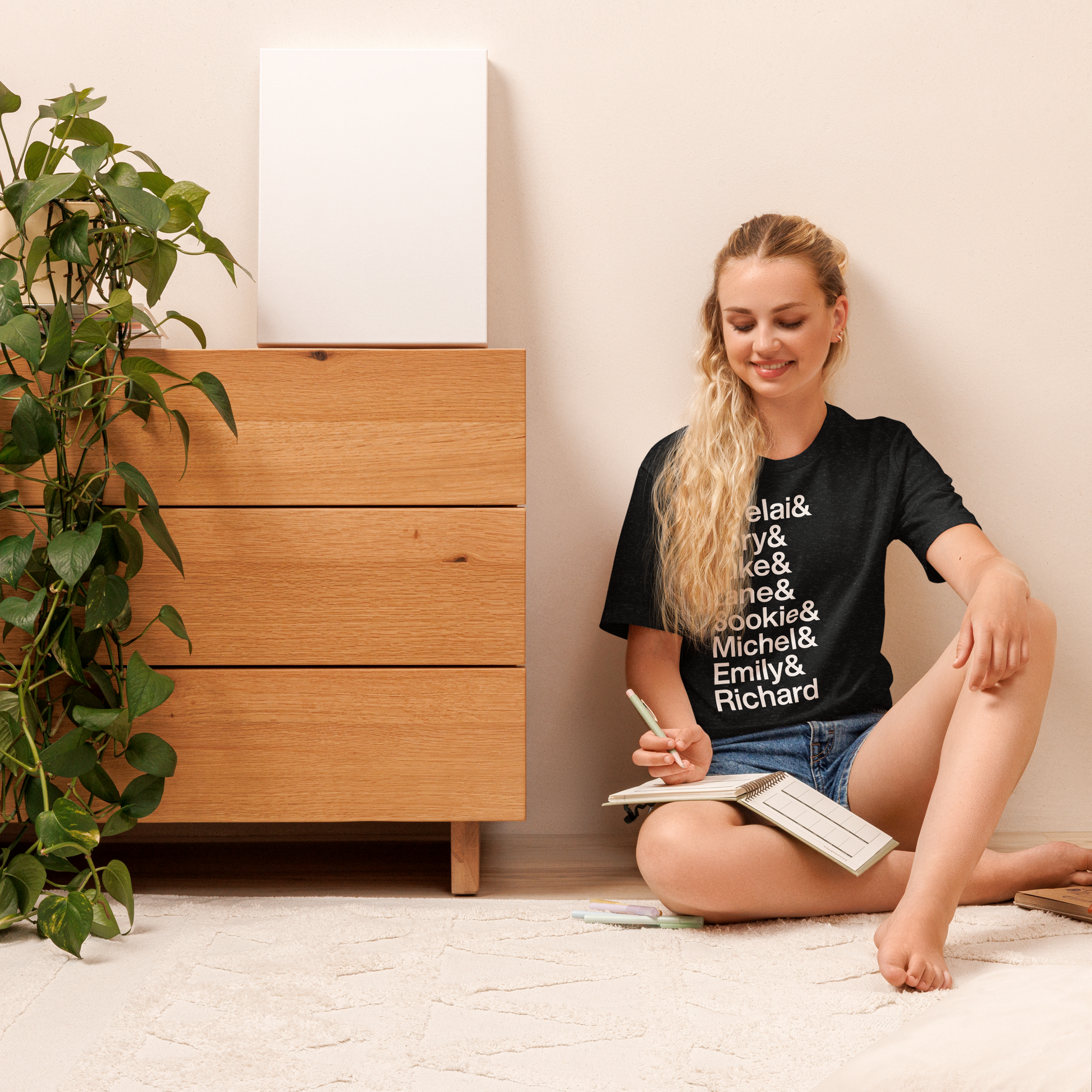 Young woman sitting on the ground wearing a black t-shirt reading Lorelai and Rory and Luke and Lane and Sookie and Michel and Emily and Richard