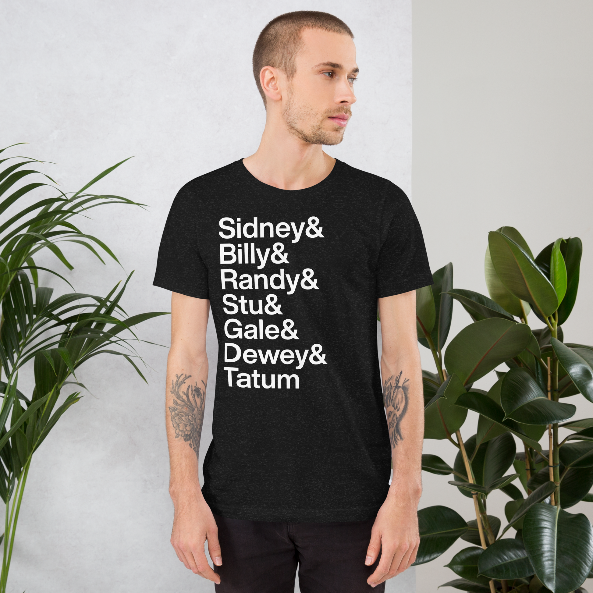 Young tattooed man wearing a black t-shirt with lettering reading "Sidney and Billy and Randy and Stu and Gale and Dewey and Tatum"
