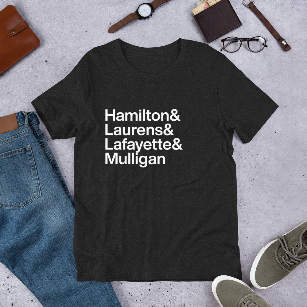 black t-shirt with white lettering reading Hamilton and Laurens and Lafayette and Mulligan on the ground with other apparel