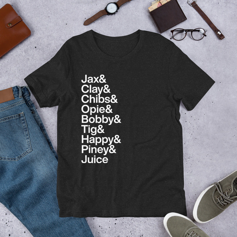 black t-shirt with white lettering reading Jax and Clay and Chibs and Opie and Bobby and Tig and Happy and Piney and Juice on ground amidst apparel