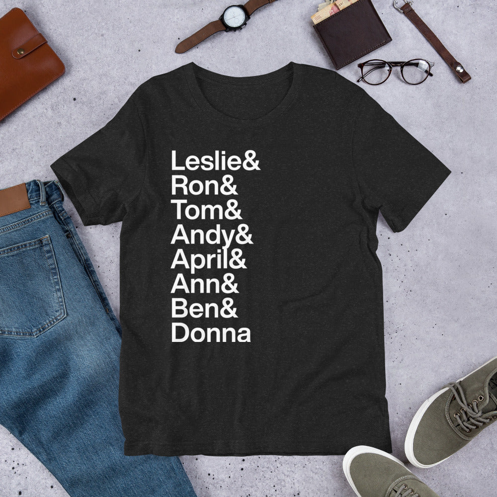 black t-shirt with white lettering reading Leslie and Ron and Tom and Andy and April and Ann and Ben and Donna on the ground amidst other apparel