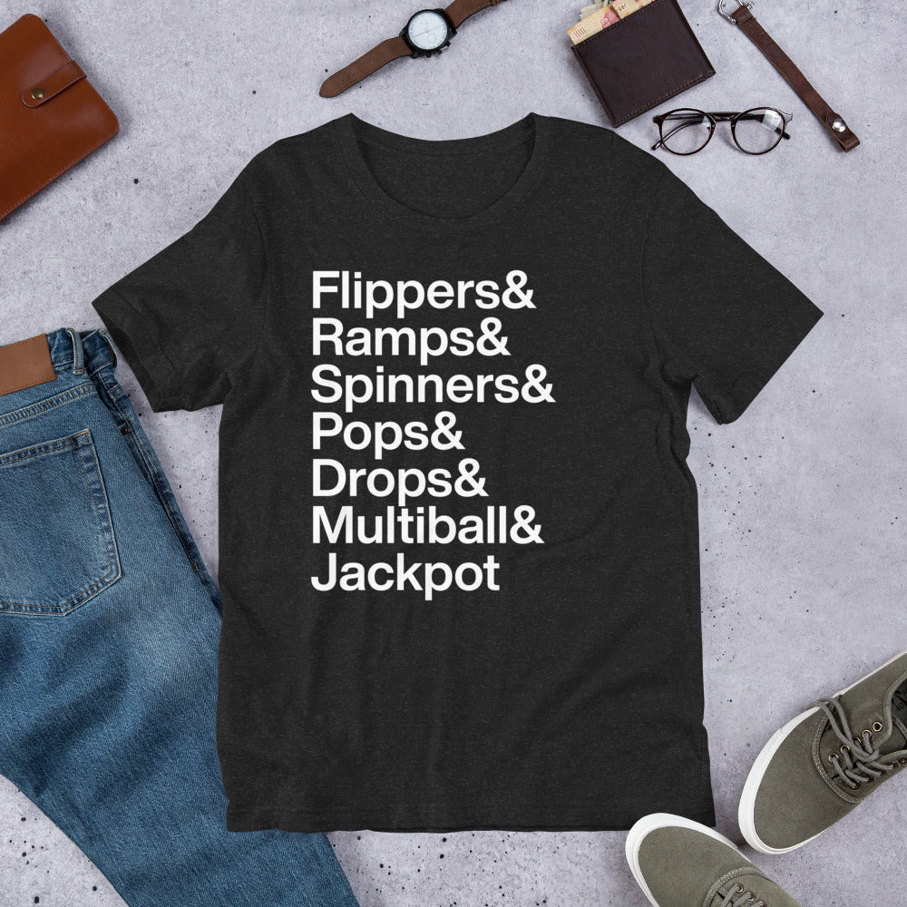black t-shirt with white lettering reading Flippers and Ramps and Spinners and Pops and Drops and Multiball and Jackpot on the ground amidst apparel