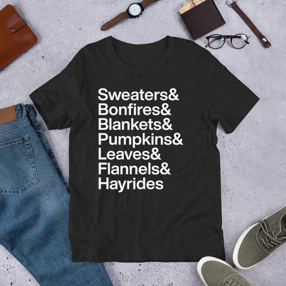 black t-shirt with white text reading "Sweaters and Bonfires and Blankets and Pumpkins and Leaves and Flannels and Hayrides" on ground with other clothing items