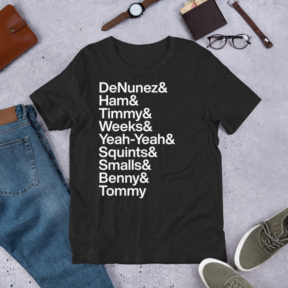 black t-shirt with white lettering depicting the characters of the Sandlot on ground next to other clothing