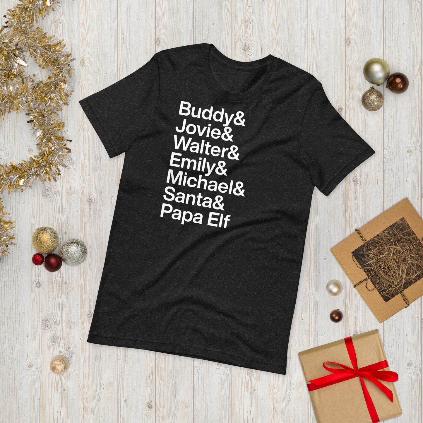  black t-shirt with white text reading Buddy and Jovie and Walter and Emily and Michel and Santa and Papa Elf on ground amidst other holiday material