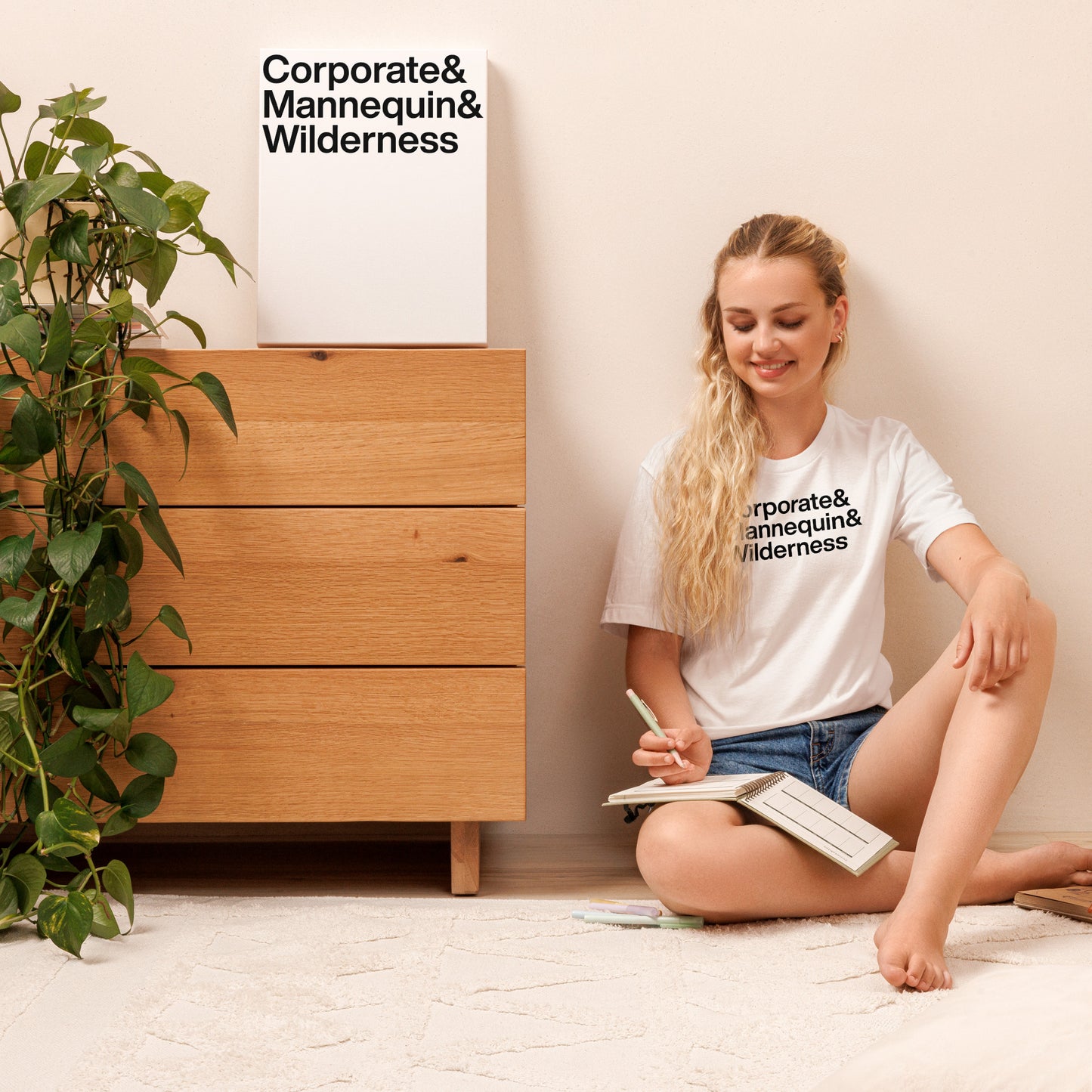 Woman sitting on the floor reading a book with a wooden dresser and plant in the background.