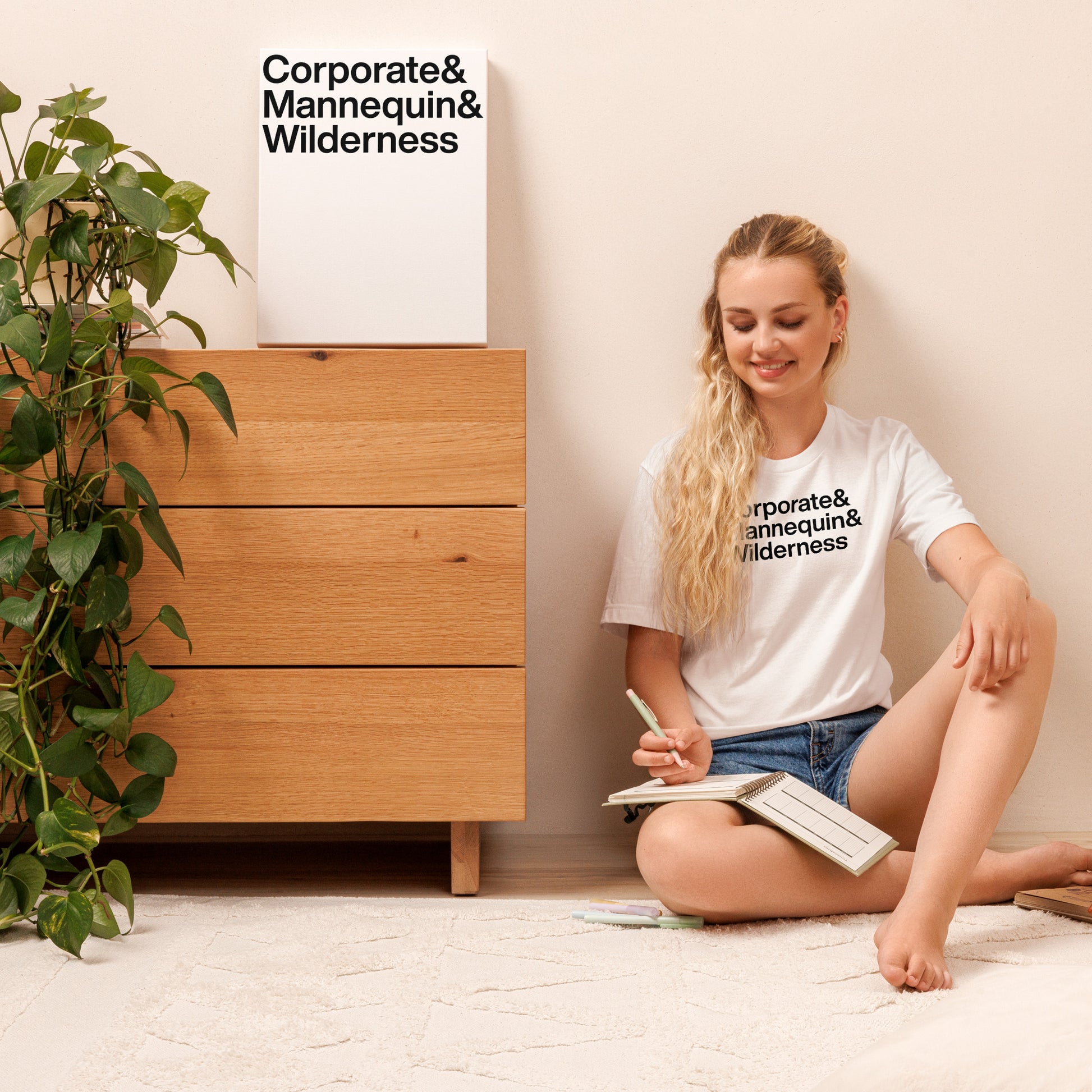 Woman sitting on the floor reading a book with a wooden dresser and plant in the background.